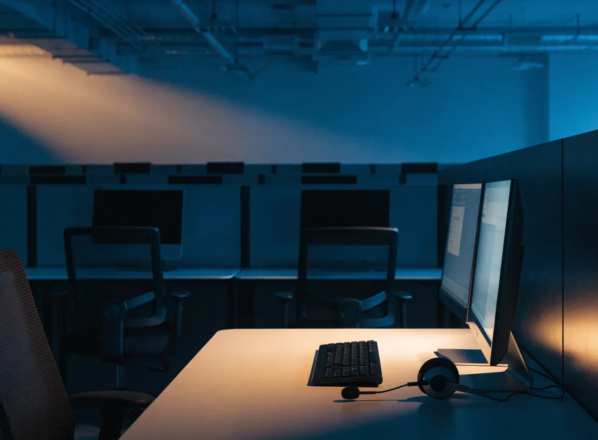 Puesto de call center 24 horas iluminado durante el turno de noche con auriculares y pantallas encendidas