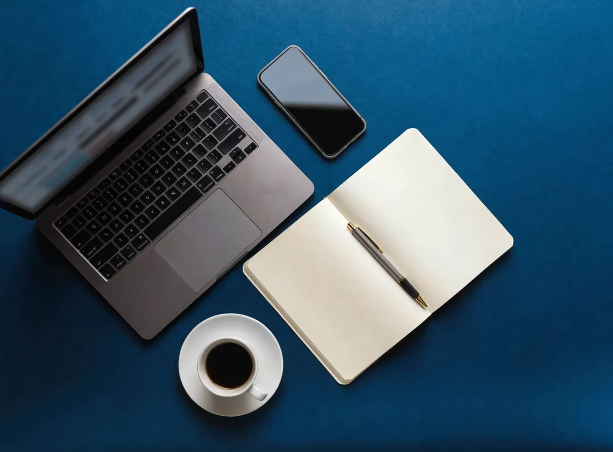 Vista cenital de una mesa de planificación de desarrollo comercial B2B con portátil, libreta y móvil